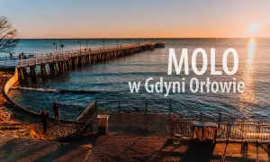 Zachód słońca nad morzem w dzielnicy Gdyni z molo. Długie molo w Orłowie, spokojne fale i dwie osoby na plaży.