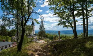 Widok na kościół i krzyż na wzgórzu w **śnieżnicki park krajobrazowy**. W tle rozciąga się malownicza dolina.