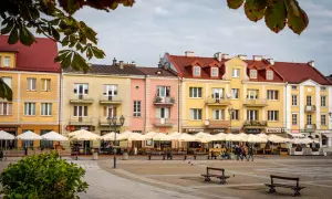 Kolorowe kamienice przy Rynku Kościuszki w Białymstoku, z ogródkami kawiarnianymi i ludźmi spacerującymi po placu.
