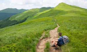Wędrowiec odpoczywa na szlaku, podziwiając zielone połoniny. Idealne Bieszczady na weekend.