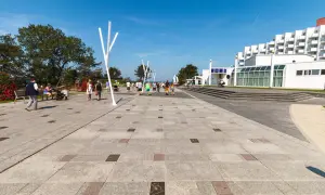 Spacerowicze na alei gwiazd w Międzyzdrojach, z widocznym hotelem i nowoczesnymi instalacjami.