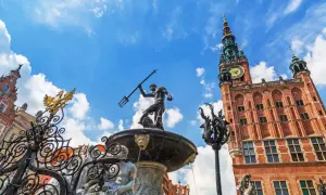 Fontanna Neptuna i Ratusz Głównego Miasta na tle błękitnego nieba z chmurami. Gdańsk Stare Miasto w pełnym słońcu.