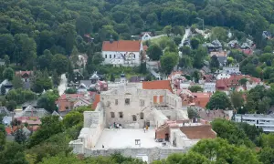 Ruiny zamkowe na wzgórzu, otoczone zielenią i zabudowaniami miasteczka.