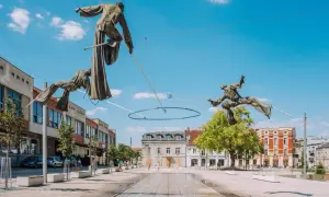 Rzeźby akrobatów na linach nad placem w Częstochowa stare miasto. W tle budynki i błękitne niebo.
