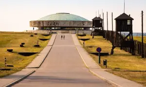 Droga prowadzi do Mauzoleum na terenie byłego obozu Majdanek. Dwie postacie idą w stronę monumentalnej budowli.