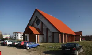 Nowoczesny kościół w Jarosławcu z pomarańczowym dachem, otoczony parkingiem z kilkoma samochodami.