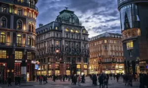 Wieczorny plac w Wiedniu, z pięknymi kamienicami i nowoczesnym budynkiem. Ludzie spacerują po oświetlonym deptaku, czuć atmosferę Wiednia Erdberg.