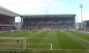 Mecz piłki nożnej na stadionie Ewood Park, pełne trybuny kibiców, zawodnicy na zielonej murawie.