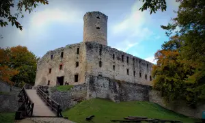 Kamienny zamek w Libiążu, z wieżą i drewnianym mostem, otoczony jesiennymi drzewami.