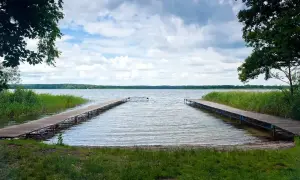 Dwa drewniane pomosty w Boszkowie zapraszają do wodnych atrakcji. Jezioro, trzciny i chmury tworzą malowniczy krajobraz.