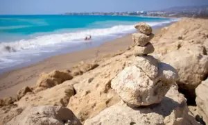Kamienna wieża na plaży w Kato Pafos, z turkusowym morzem i falami w tle.