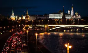Wieczorny ruch uliczny w Moskwie, z oświetlonym Kremlem i rzeką w tle.