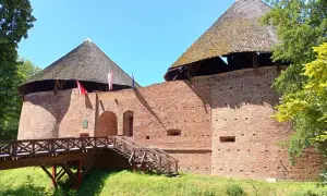 Zamek międzyrzecz z drewnianym mostem i schodami prowadzącymi do ceglanych baszt pod strzechą.