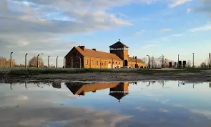 Odbicie ceglanego baraku z wieżą strażniczą w kałuży. To miejsce, gdzie jest Auschwitz, przypomina o historii.