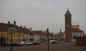 Rynek w Pułtusku z charakterystyczną wieżą. Kolorowe kamienice i zaparkowane samochody tworzą malowniczy widok.