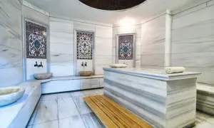 Wnętrze hamamu z marmurowymi ścianami, ozdobnymi kafelkami i kamiennymi misami.