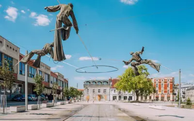 Rzeźby akrobatów na linach nad placem w Częstochowa stare miasto. W tle budynki i błękitne niebo.
