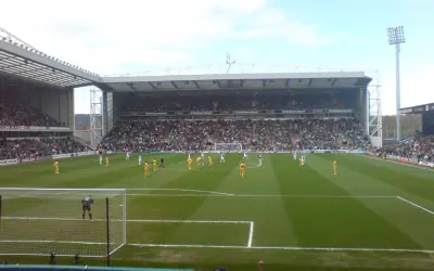 Mecz piłki nożnej na stadionie Ewood Park, pełne trybuny kibiców, zawodnicy na zielonej murawie.
