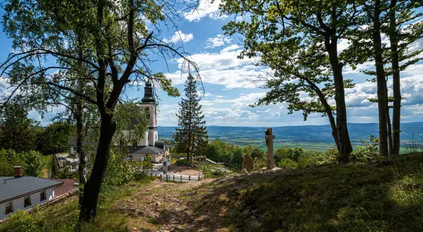 Widok na kościół i krzyż na wzgórzu w **śnieżnicki park krajobrazowy**. W tle rozciąga się malownicza dolina.