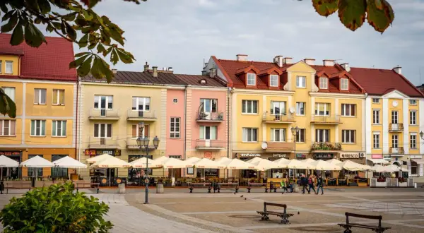 Kolorowe kamienice przy Rynku Kościuszki w Białymstoku, z ogródkami kawiarnianymi i ludźmi spacerującymi po placu.