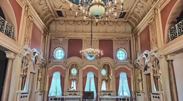 Wnętrze pałacu poznańskiego z bogatymi zdobieniami, wielkimi oknami i dwoma żyrandolami.