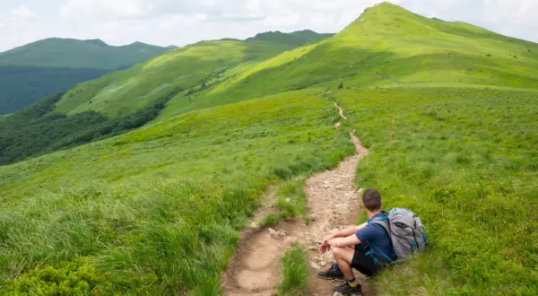 Wędrowiec odpoczywa na szlaku, podziwiając zielone połoniny. Idealne Bieszczady na weekend.