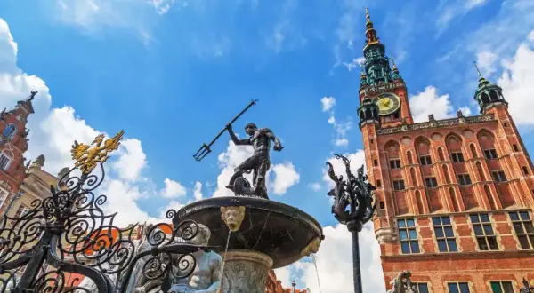 Fontanna Neptuna i Ratusz Głównego Miasta na tle błękitnego nieba z chmurami. Gdańsk Stare Miasto w pełnym słońcu.