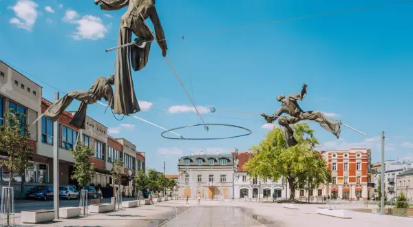Rzeźby akrobatów na linach nad placem w Częstochowa stare miasto. W tle budynki i błękitne niebo.