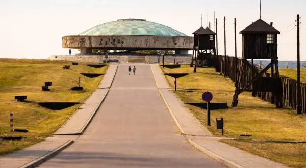 Droga prowadzi do Mauzoleum na terenie byłego obozu Majdanek. Dwie postacie idą w stronę monumentalnej budowli.