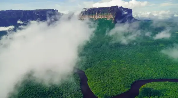 Mgliste chmury otulają zielony las i krętą rzekę, odsłaniając majestatyczne góry. Widok jak z **Angel Falls**.