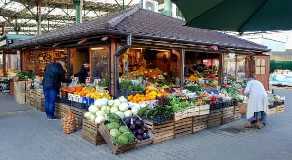 Kolorowy stragan na Kleparzu pełen świeżych warzyw i owoców. Klienci wybierają produkty, tworząc tętniącą życiem scenę.