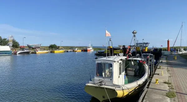 Portowe atrakcje: łodzie rybackie, w tym "Katy Rybackie", cumują przy nabrzeżu. Kaczka pływa w spokojnej wodzie.