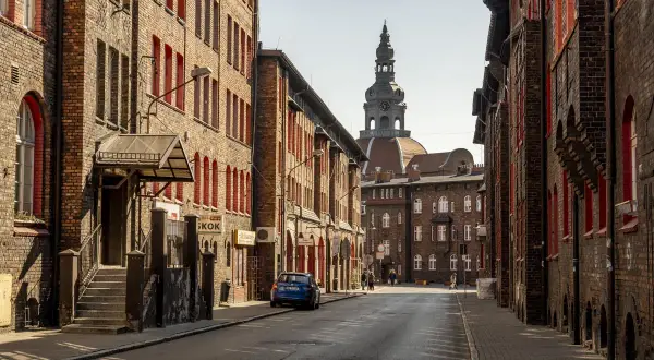 Charakterystyczna zabudowa Nikiszowca z ceglanymi kamienicami i wieżą kościelną w tle.