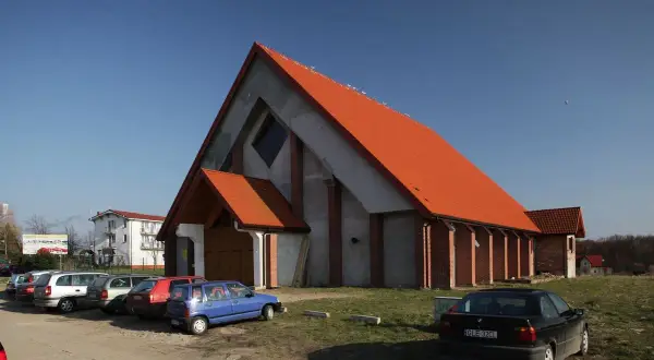 Nowoczesny kościół w Jarosławcu z pomarańczowym dachem, otoczony parkingiem z kilkoma samochodami.