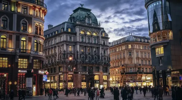 Wieczorny plac w Wiedniu, z pięknymi kamienicami i nowoczesnym budynkiem. Ludzie spacerują po oświetlonym deptaku, czuć atmosferę Wiednia Erdberg.