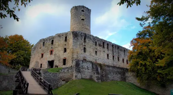 Kamienny zamek w Libiążu, z wieżą i drewnianym mostem, otoczony jesiennymi drzewami.