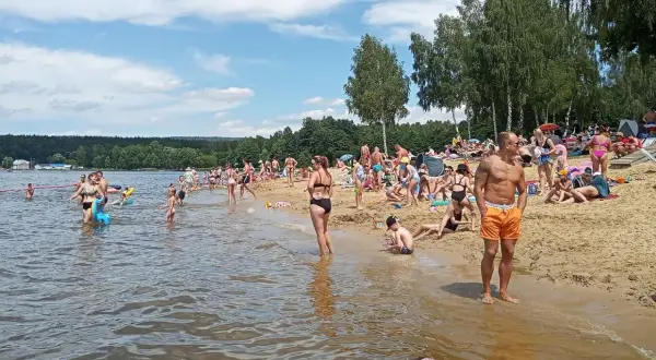 Tłumy ludzi korzystają z kąpieliska, plaży i wodnych atrakcji w słoneczny dzień.