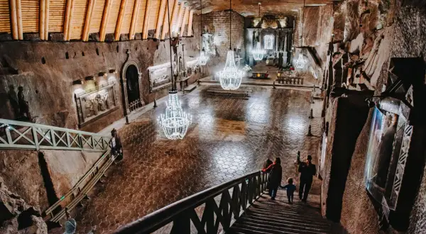 Wielka komora w kopalni soli Wieliczka, z kryształowymi żyrandolami i turystami schodzącymi po schodach. Sprawdź kopalnia soli Wieliczka cennik.