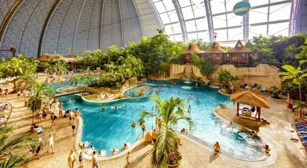 Wielki tropikalny basen pod kopułą, z palmami, domkami i ludźmi. Sprawdź nasz tropical island cennik, by zaplanować wakacje!