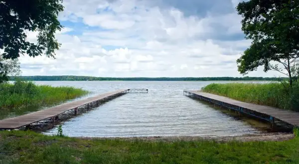 Dwa drewniane pomosty w Boszkowie zapraszają do wodnych atrakcji. Jezioro, trzciny i chmury tworzą malowniczy krajobraz.