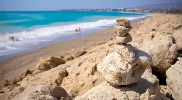 Kamienna wieża na plaży w Kato Pafos, z turkusowym morzem i falami w tle.