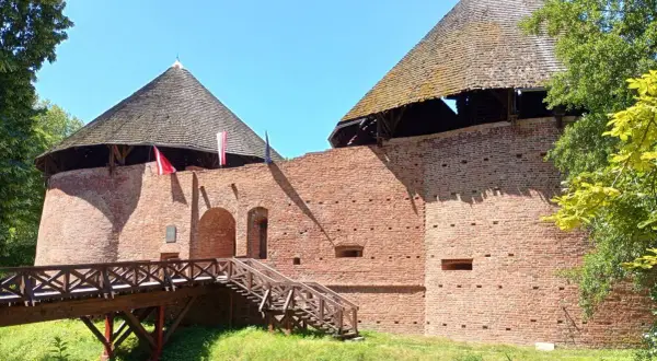 Zamek międzyrzecz z drewnianym mostem i schodami prowadzącymi do ceglanych baszt pod strzechą.