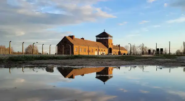 Odbicie ceglanego baraku z wieżą strażniczą w kałuży. To miejsce, gdzie jest Auschwitz, przypomina o historii.
