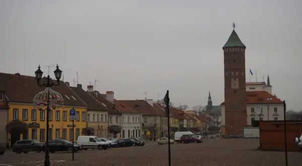 Rynek w Pułtusku z charakterystyczną wieżą. Kolorowe kamienice i zaparkowane samochody tworzą malowniczy widok.