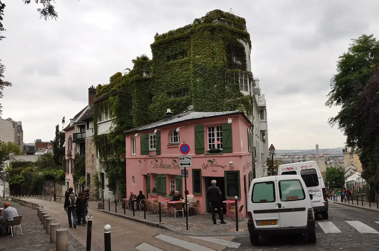 Urokliwa ulica na Montmartre z różową kawiarnią La Maison Rose i budynkiem obrośniętym bluszczem.