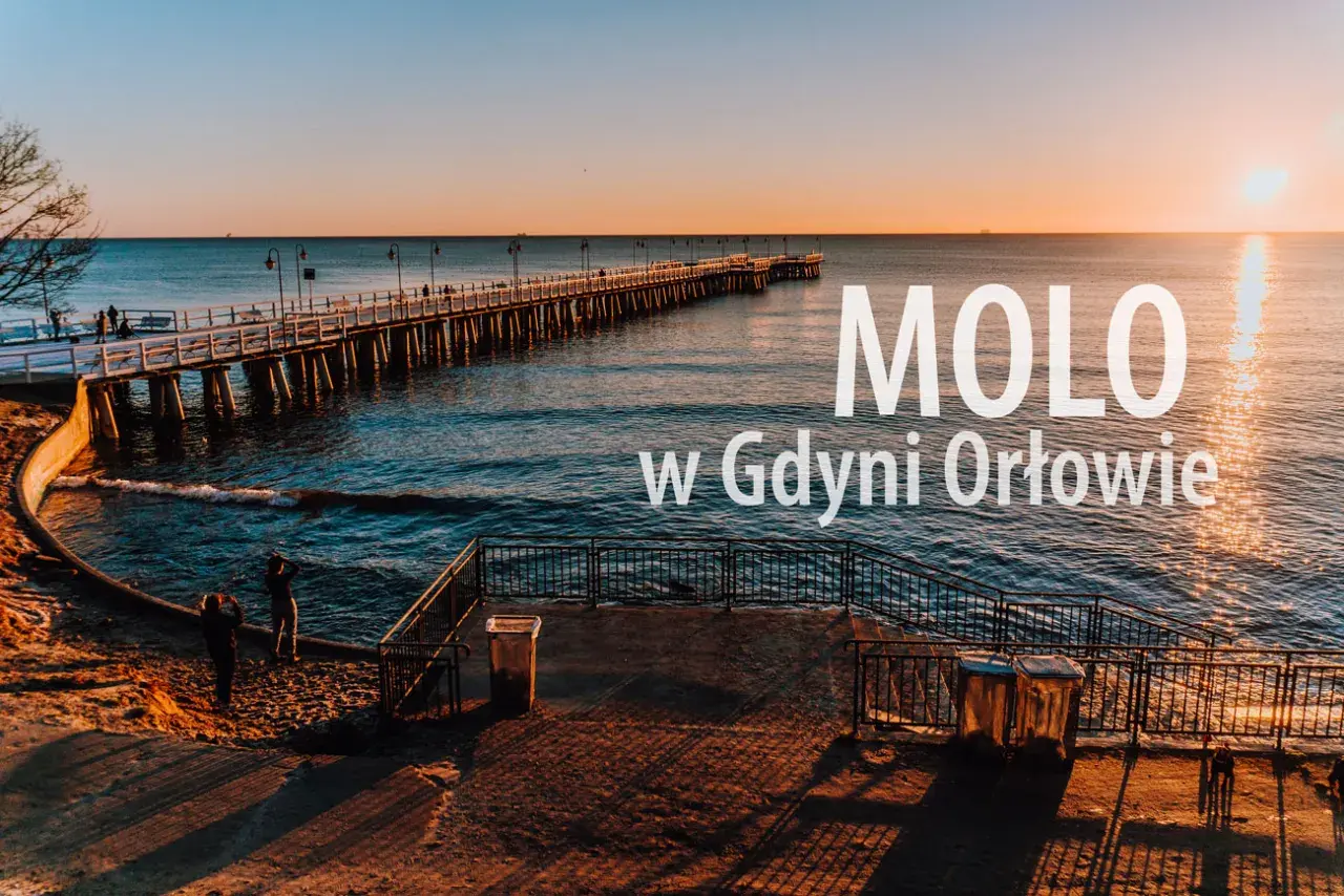 Zachód słońca nad morzem w dzielnicy Gdyni z molo. Długie molo w Orłowie, spokojne fale i dwie osoby na plaży.