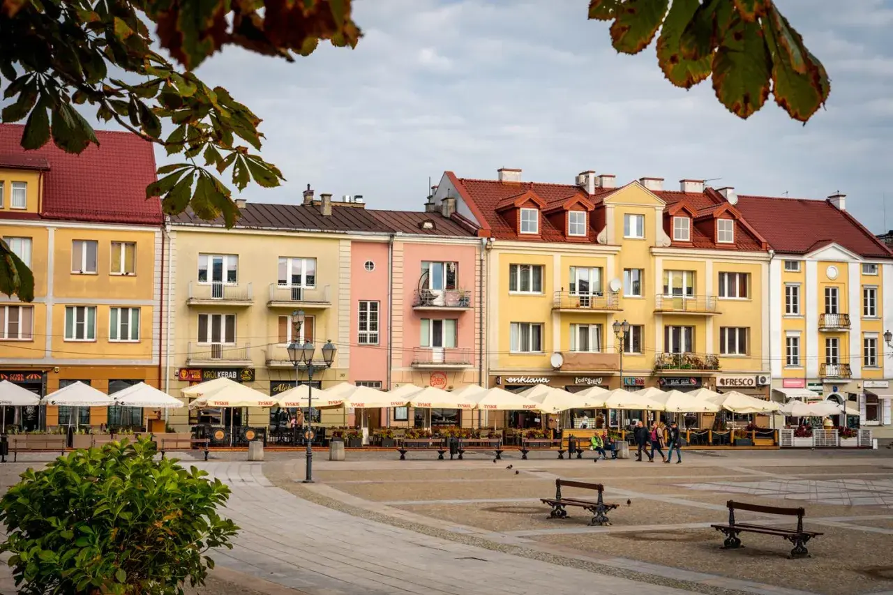 Kolorowe kamienice przy Rynku Kościuszki w Białymstoku, z ogródkami kawiarnianymi i ludźmi spacerującymi po placu.