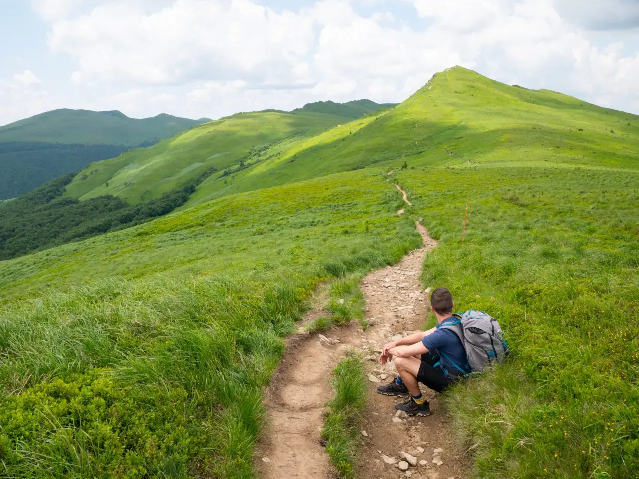 Wędrowiec odpoczywa na szlaku, podziwiając zielone połoniny. Idealne Bieszczady na weekend.