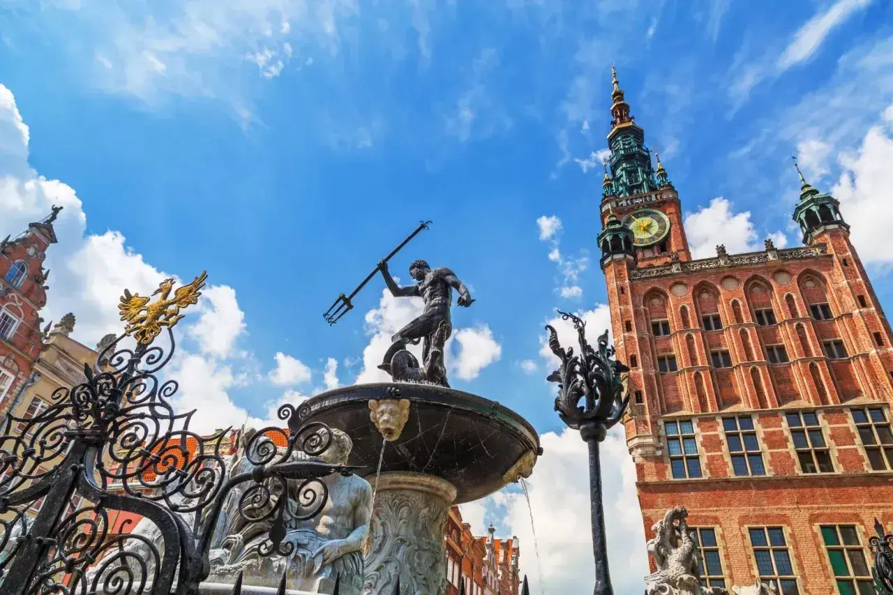 Fontanna Neptuna i Ratusz Głównego Miasta na tle błękitnego nieba z chmurami. Gdańsk Stare Miasto w pełnym słońcu.