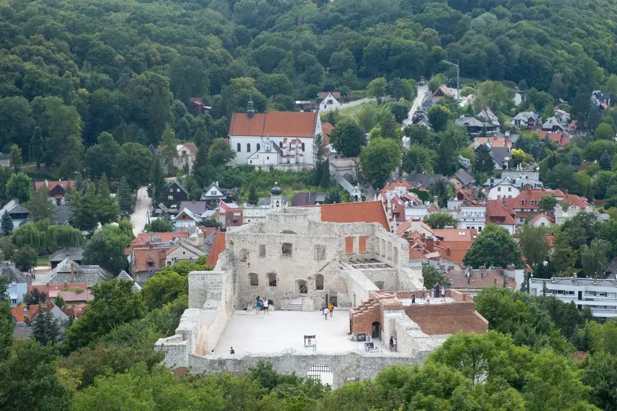 Ruiny zamkowe na wzgórzu, otoczone zielenią i zabudowaniami miasteczka.